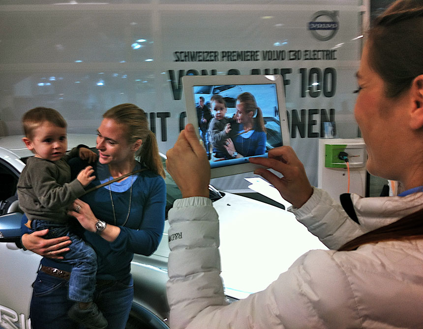 A hostess taking a picture of an interested woman holding her son using the iPad 2